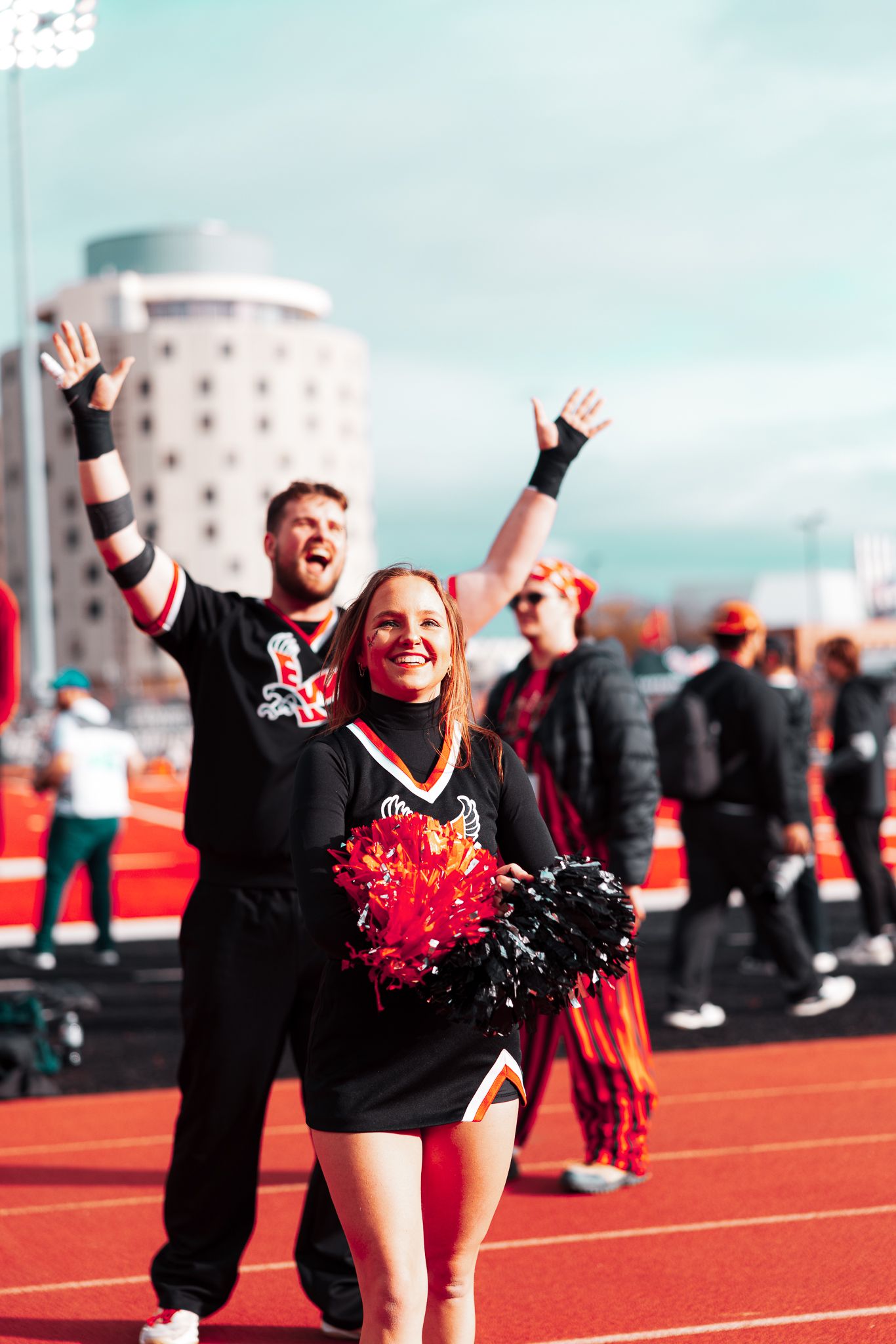 Cheerleaders in black uniforms perform energetic routines on a bright red running track during an outdoor event.
