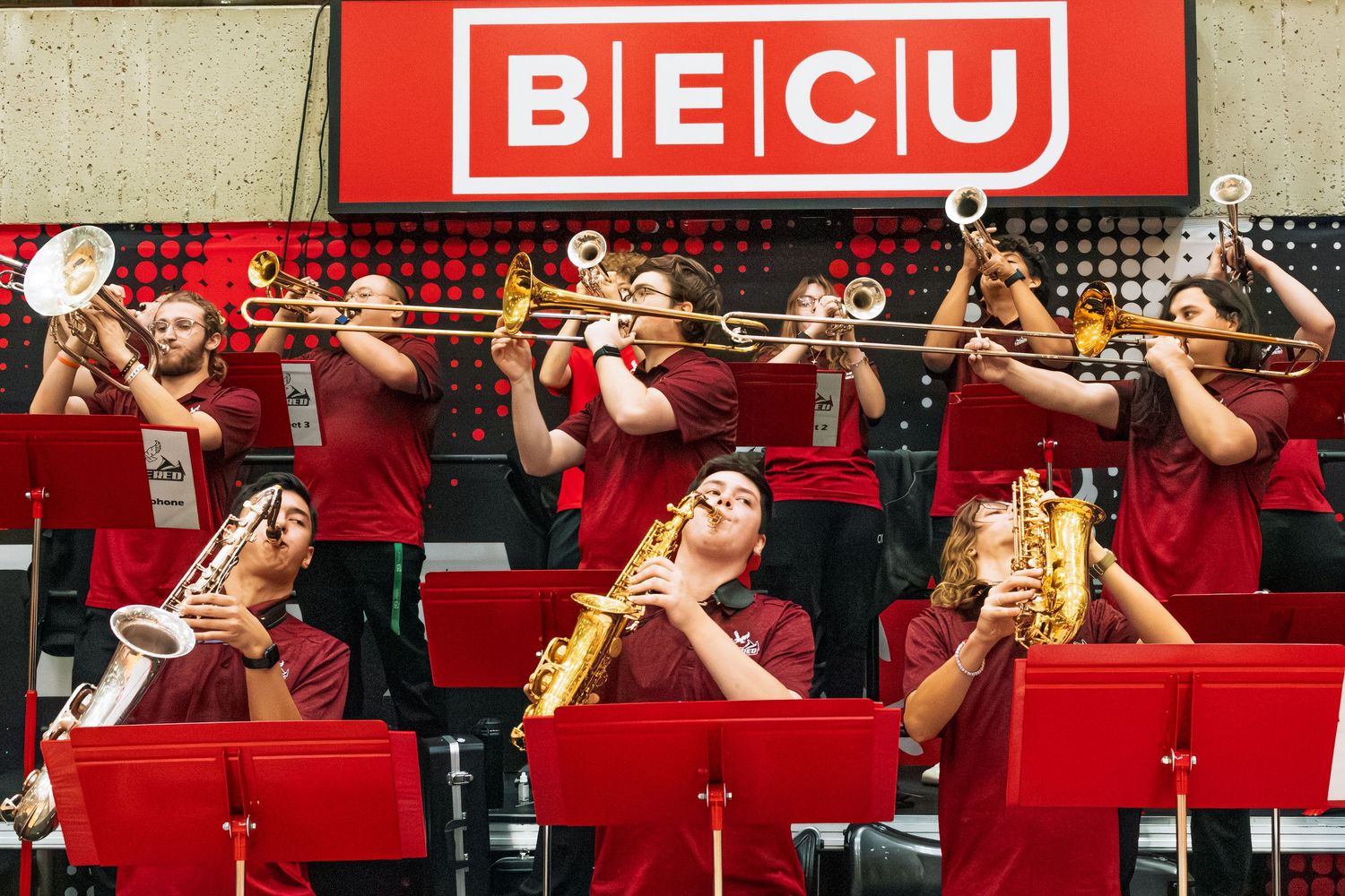Musicians in red uniforms perform with brass instruments during a concert performance on stage.