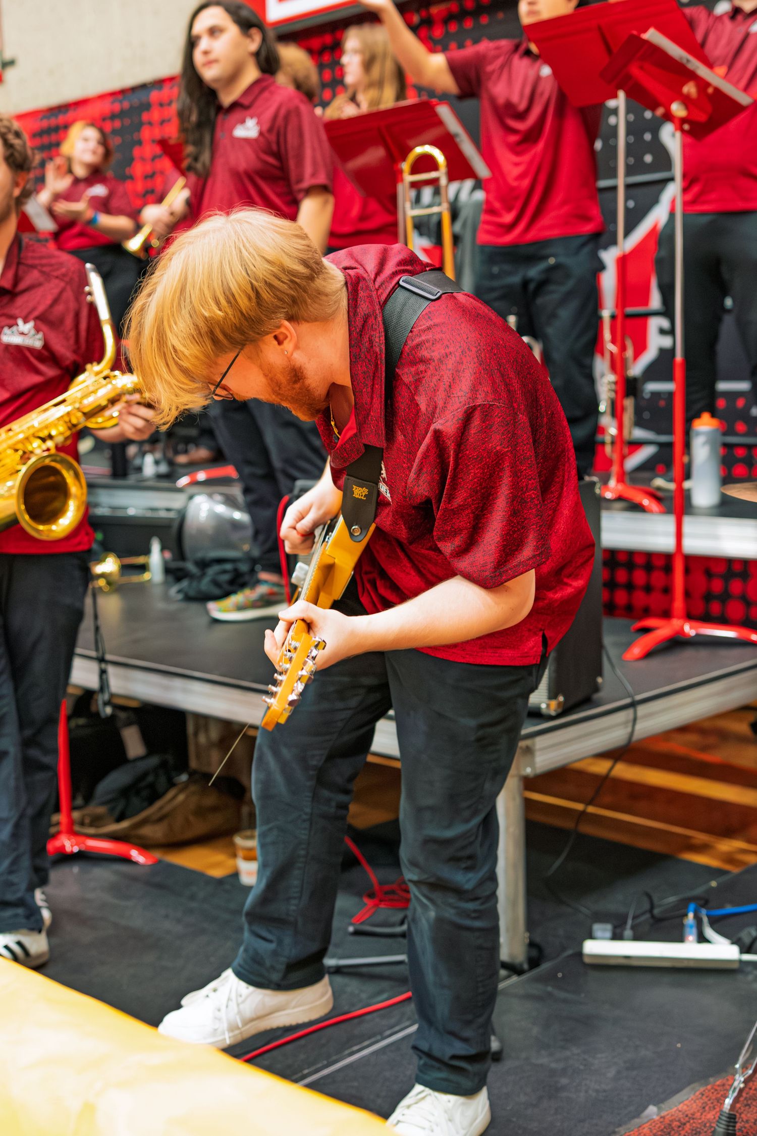 Musicians in red shirts perform in a row with brass instruments during a band performance.