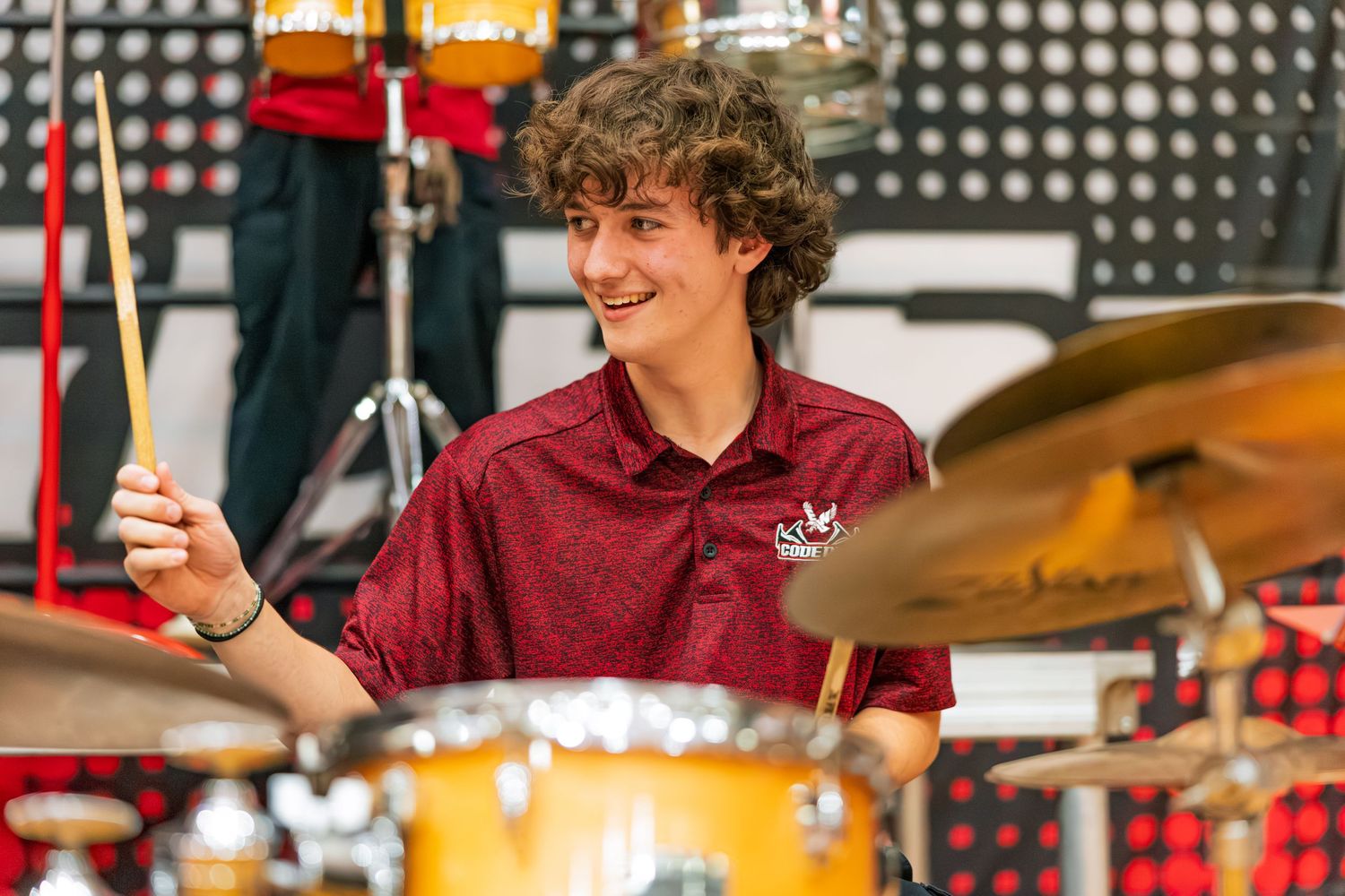 Drummer performs energetically behind a drum kit on stage with colorful lighting in the background.