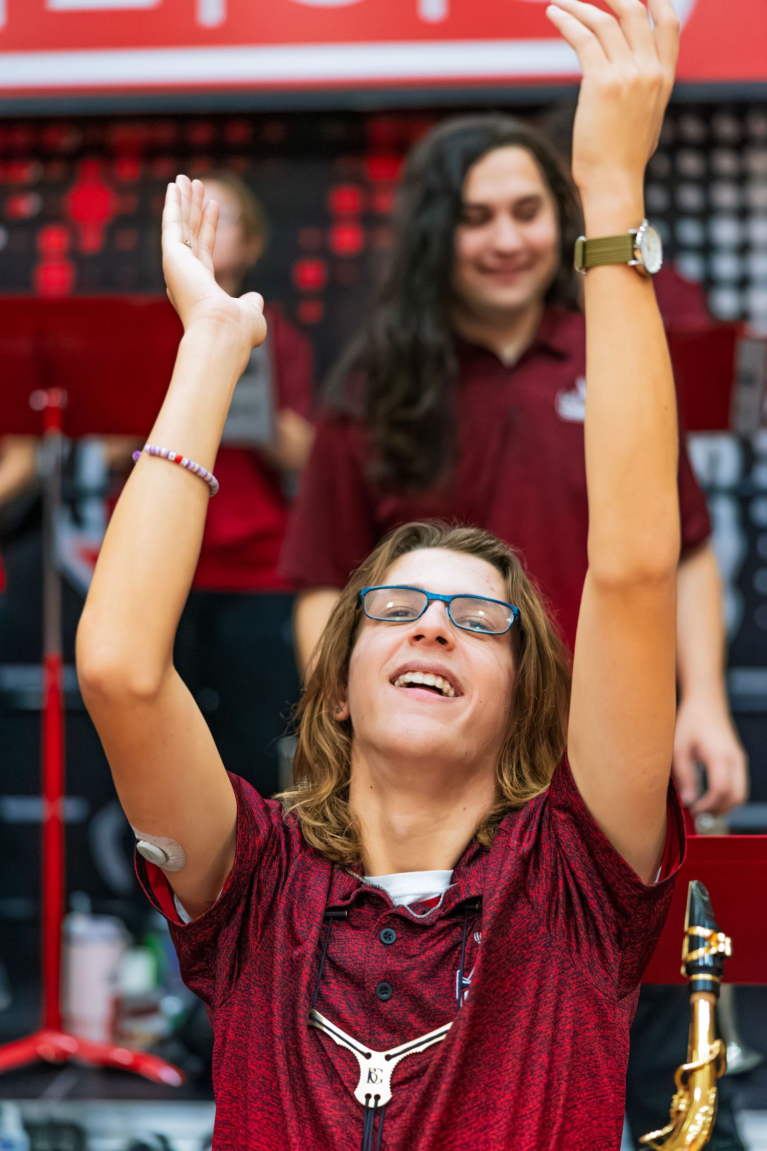 A student in maroon attire cheers enthusiastically with raised arms at a sporting event.