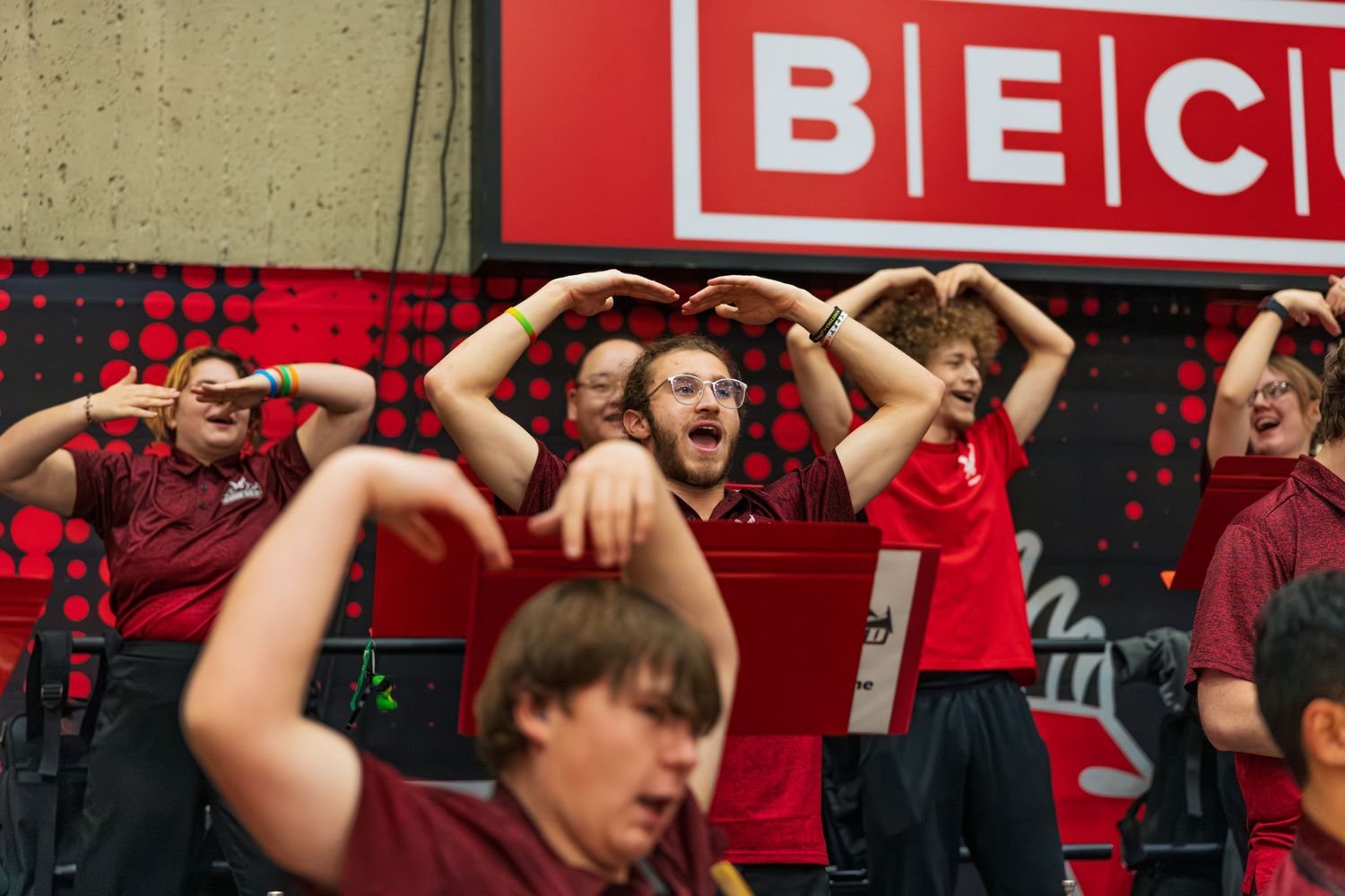 A crowd of basketball fans in red attire cheering and raising their arms in an arena during an exciting game moment.
