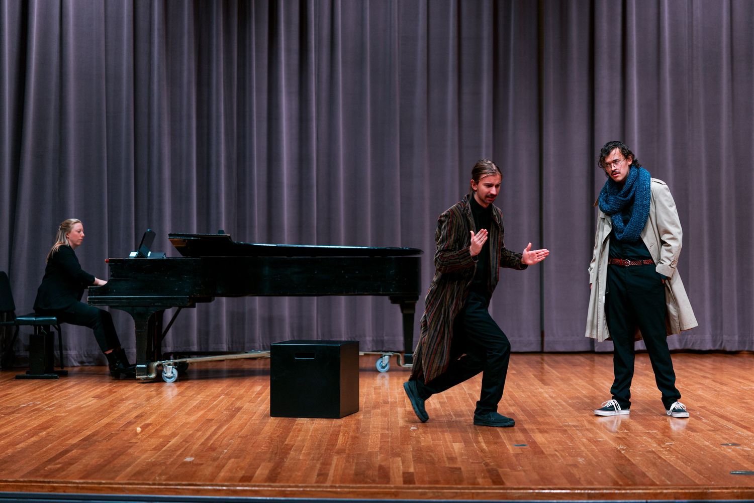 Two performers interact on a stage while a pianist plays on a grand piano in the background.