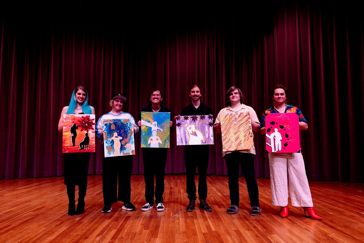 A group of performers take a bow on stage with red curtains in the background after a theater performance.