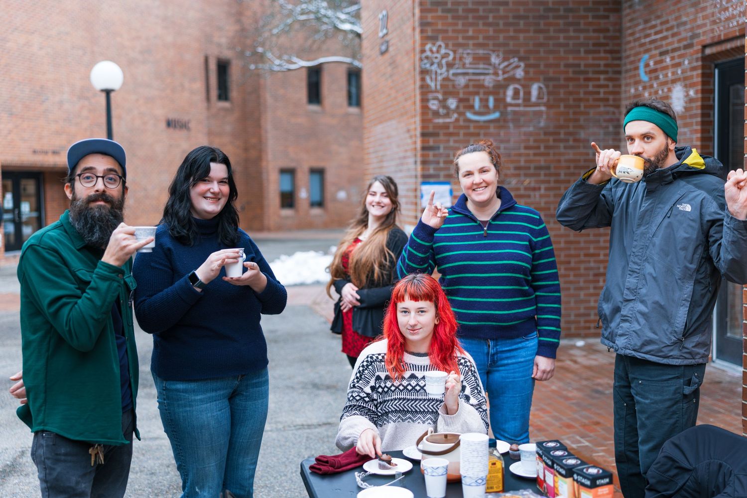 A group of people holding up beer glasses in a celebratory toast outside a brick building.