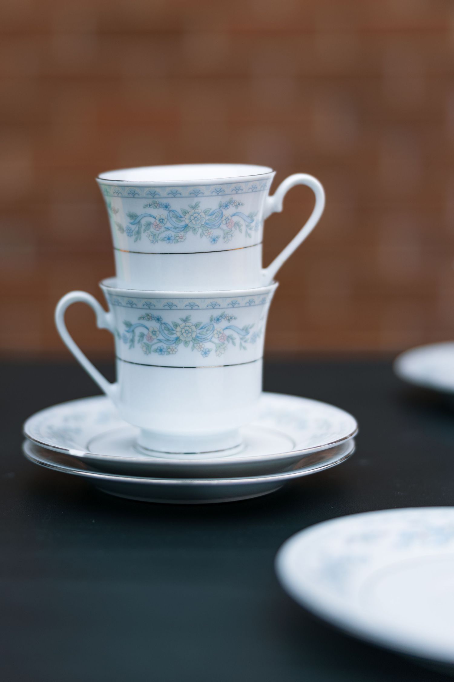 Elegant white porcelain teacup and saucer with delicate blue floral pattern stacked in artistic arrangement.