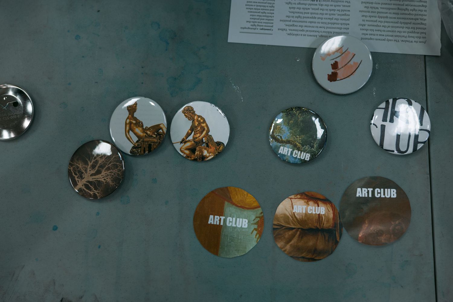 Circular pin buttons with artwork and designs displayed on a textured teal-colored surface.