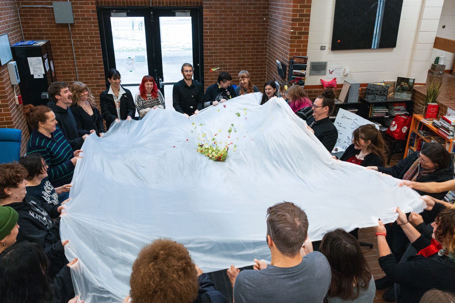 Students collaborate in a classroom activity by holding up a large white fabric sheet together.
