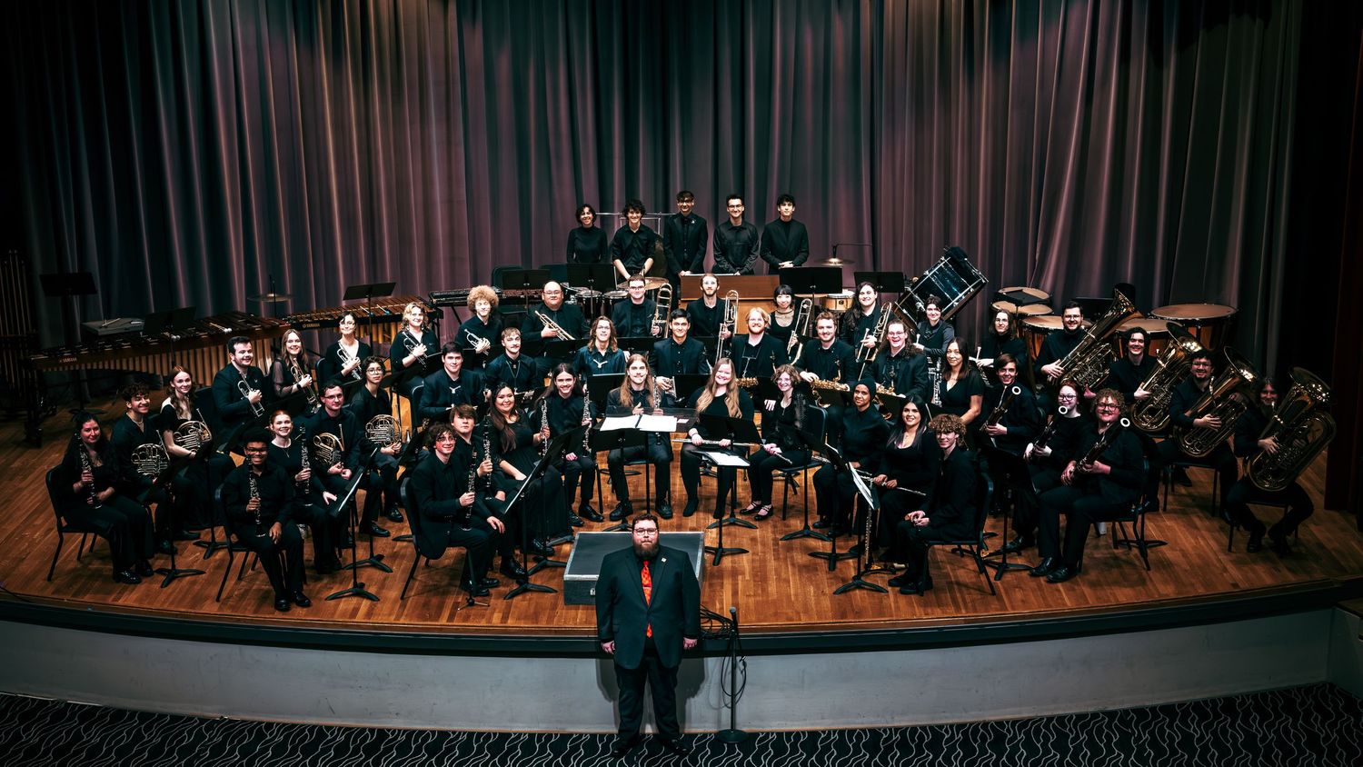 Orchestra musicians perform on stage in a concert hall with dramatic lighting and multiple panoramic views.