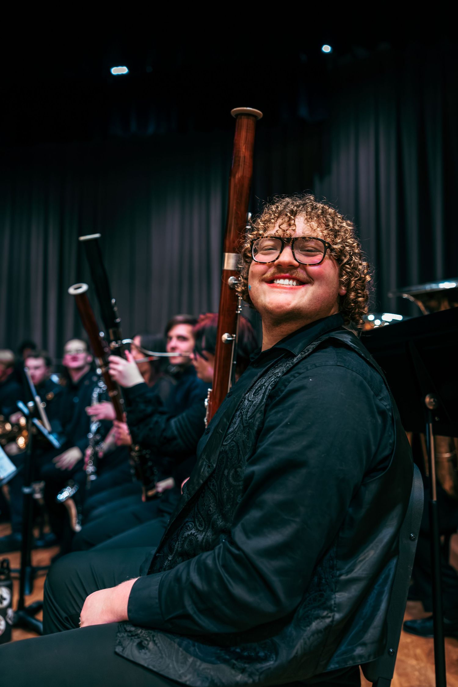 Musicians perform in black attire during an orchestral concert with bagpipes visible in the background.