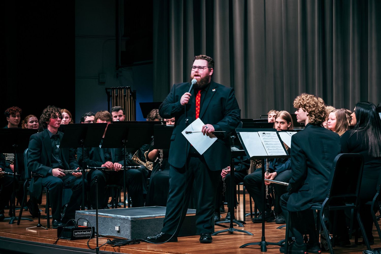 A conductor performs with a concert band on stage during a musical performance in an auditorium.