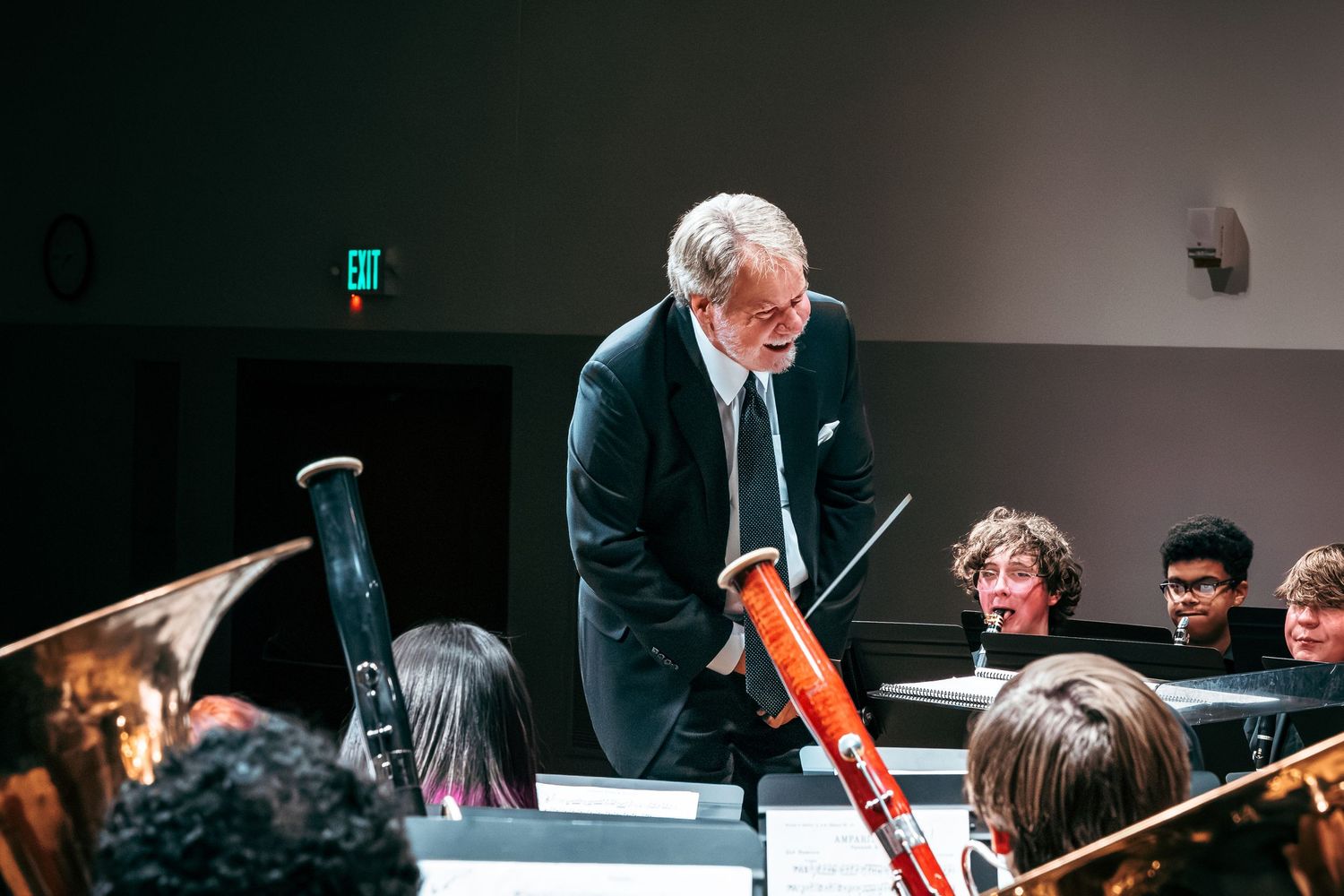 A conductor leads an orchestra during a performance while leaning forward with baton in hand.
