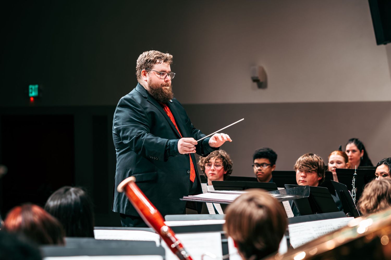 A conductor leads an orchestra during a performance in a concert hall with musicians playing various instruments.