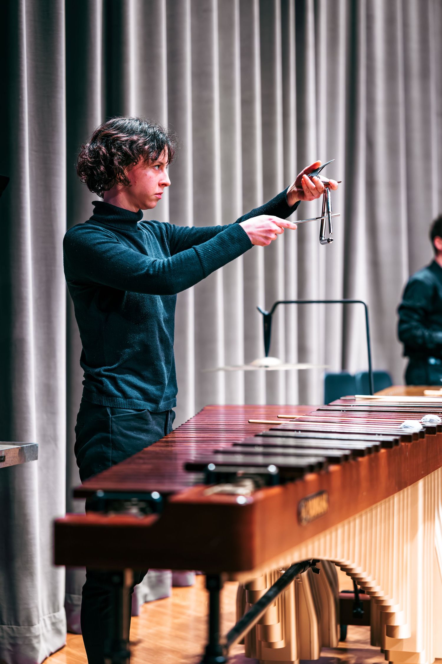Musician in black attire performs on multiple marimbas in a concert hall with white pillars in the background.
