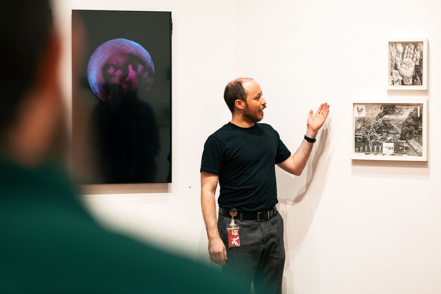A person in a black shirt examines artwork displayed on a white gallery wall.