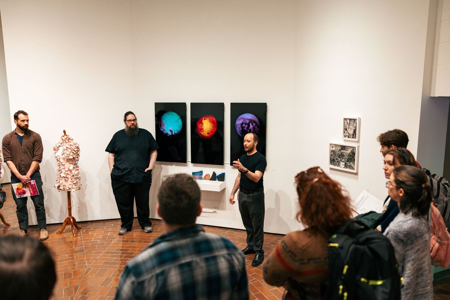 People stand in a line against a white gallery wall viewing artwork in an exhibition space.
