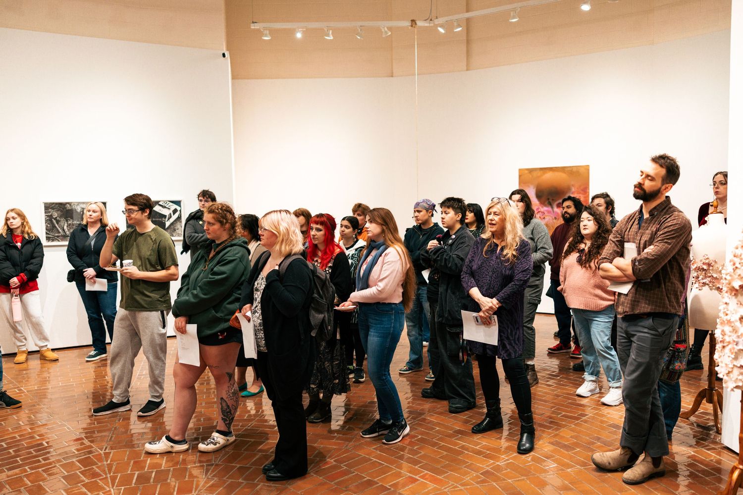 A panoramic view of people standing in a white gallery space viewing artwork displayed along the walls.