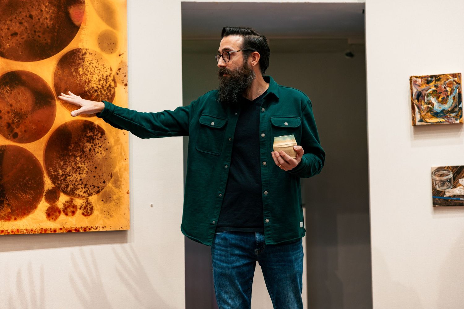 A person in a dark shirt gestures while presenting artwork displayed on gallery walls.