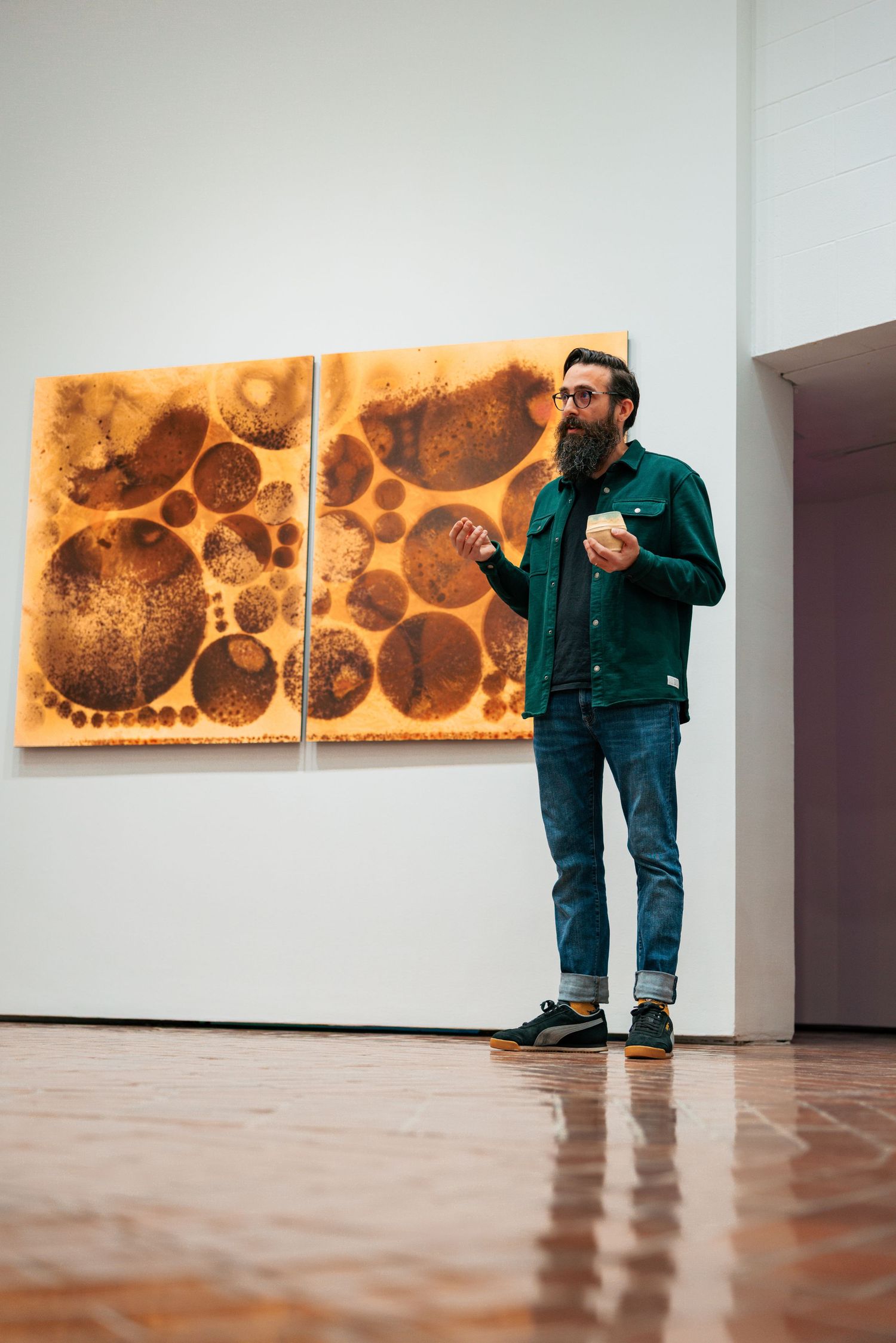 A person in green attire views abstract artwork displayed on a white gallery wall.