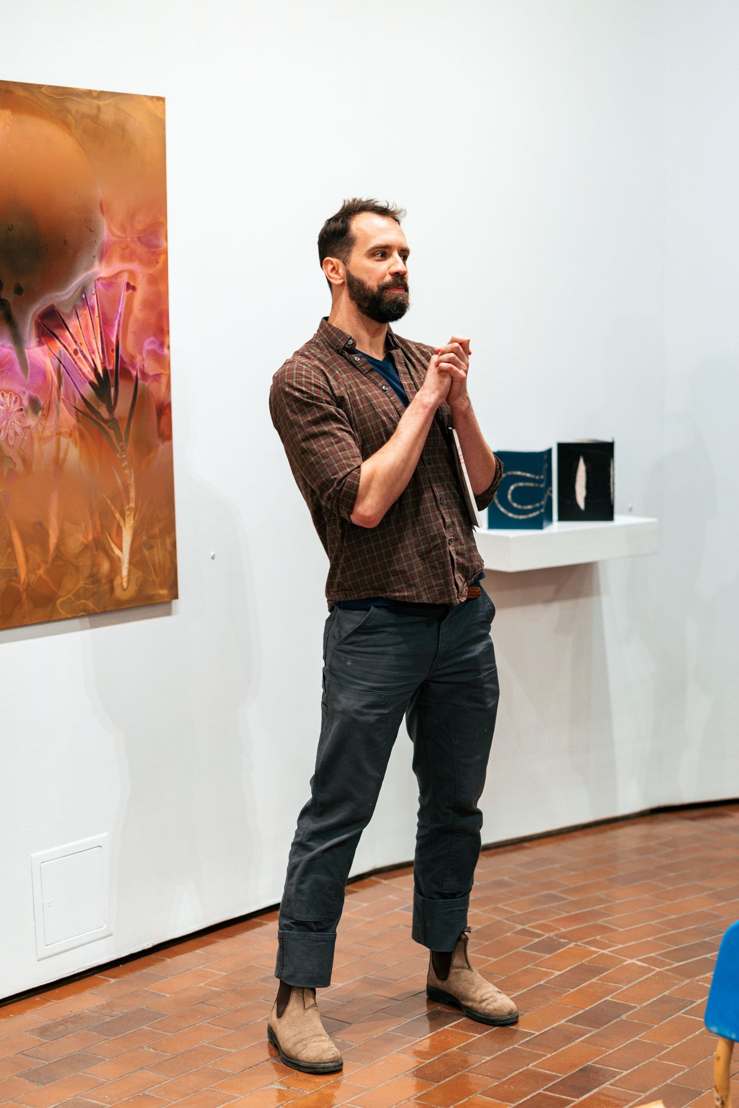 A person stands contemplatively in an art gallery with white walls displaying colorful artwork.