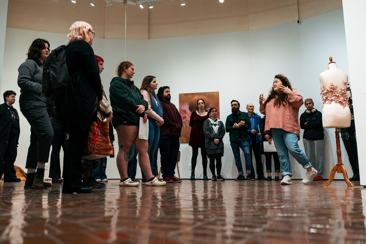 People stand in a line along a wall in a gallery or exhibition space with polished floors.