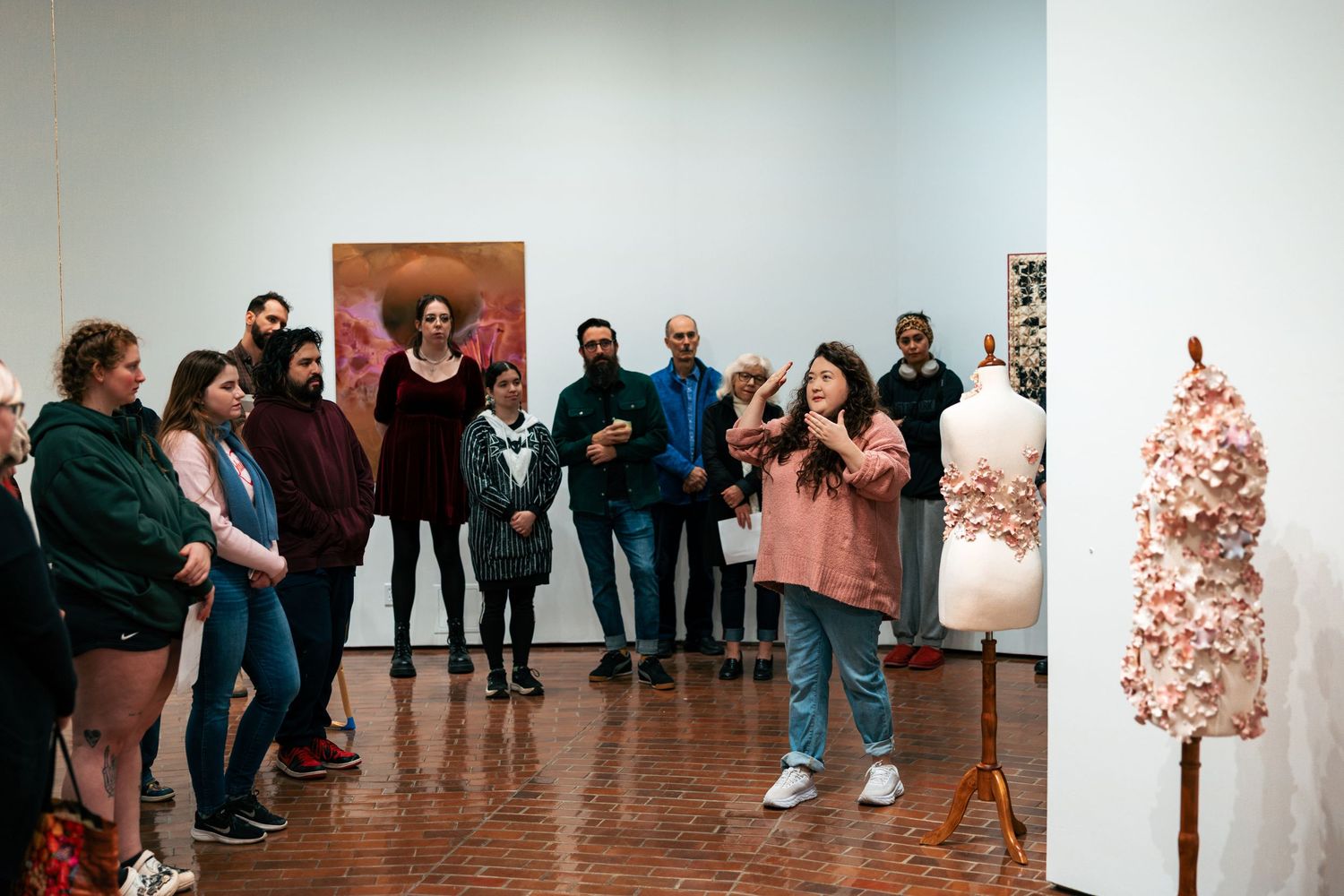 Gallery visitors observe artwork in a contemporary art exhibition space with white walls.