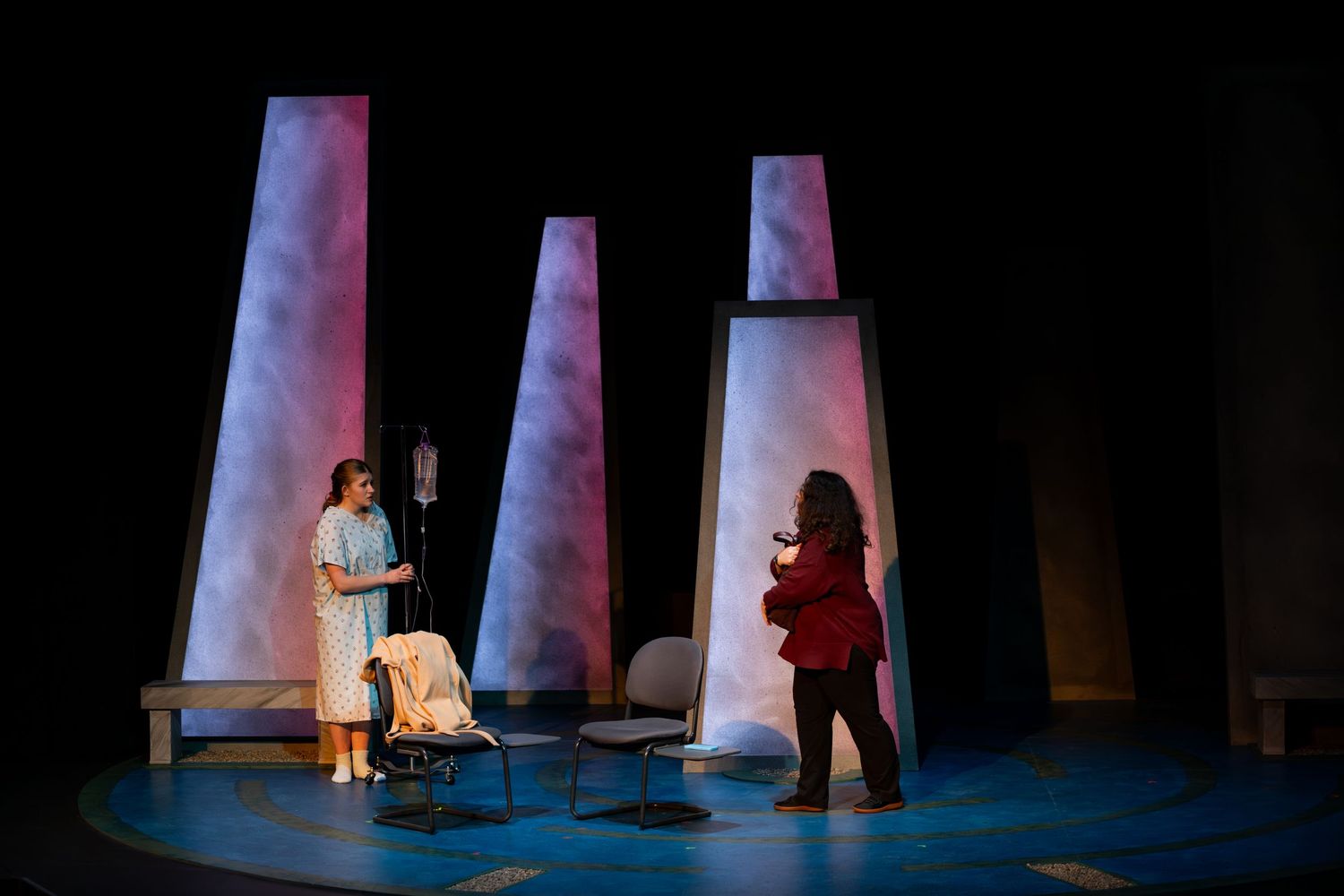 A theatrical stage performance featuring illuminated white pillars and performers in dramatic lighting.