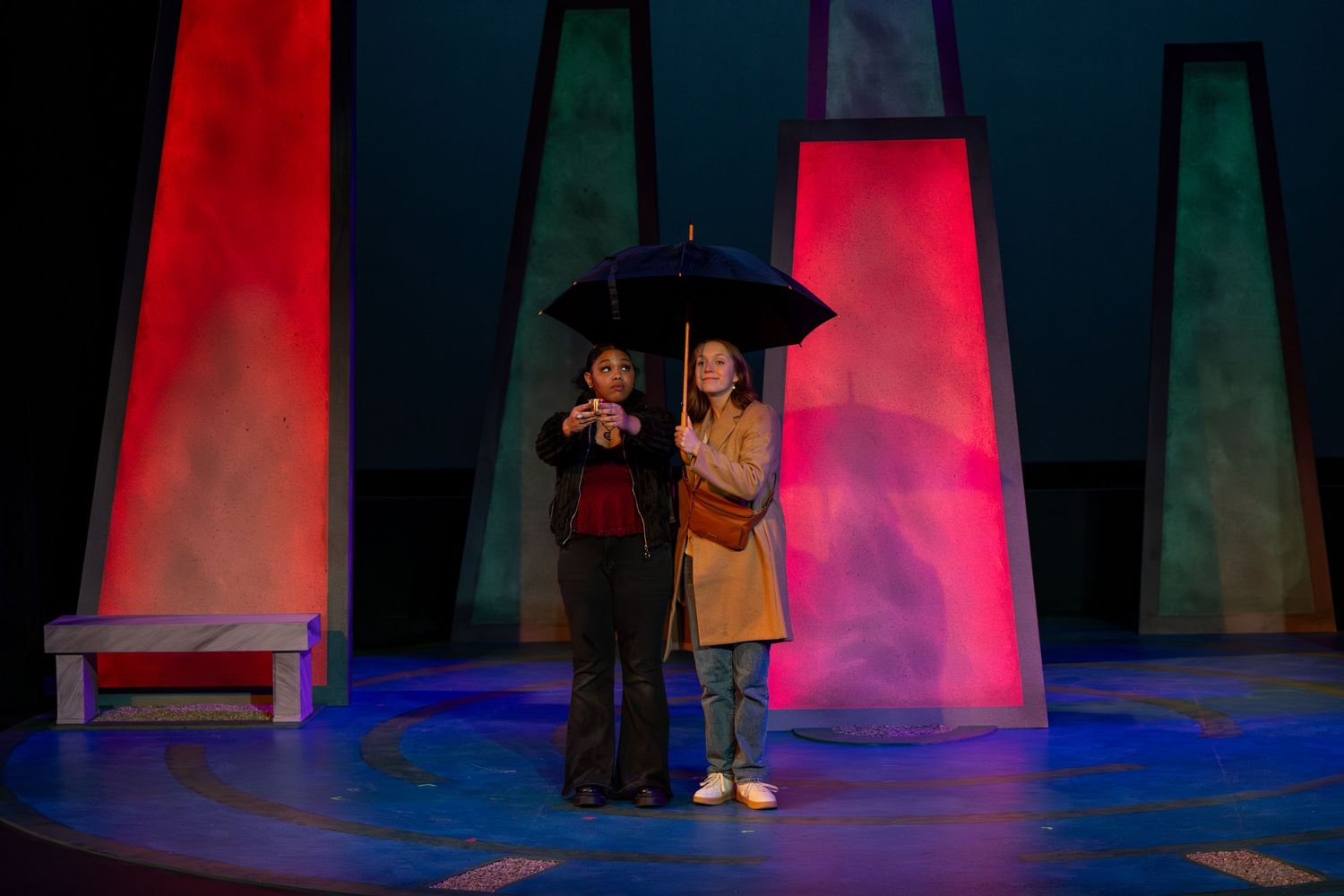Silhouetted figures stand on a theatrical stage with dramatic red and blue lighting effects.