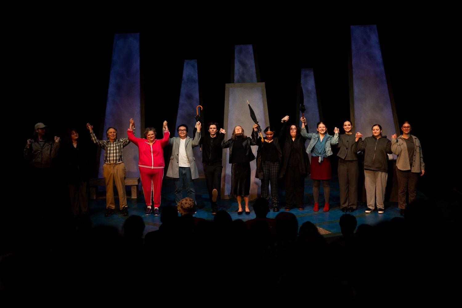 Theater performers take a bow on stage during curtain call as audience applauds their performance.