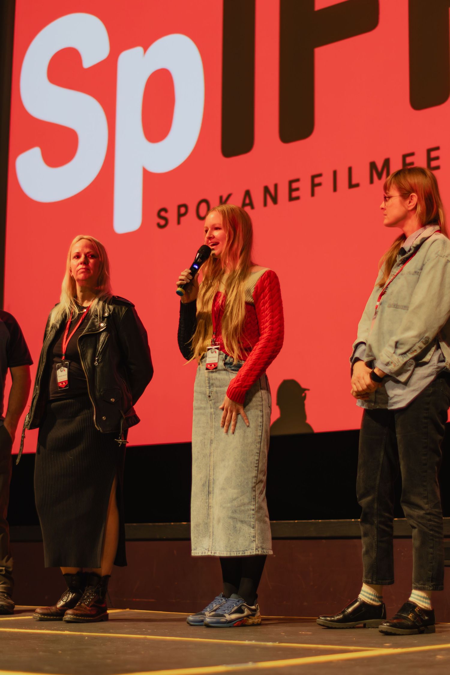 Three people stand on stage at Spokane Film Festival with large red SpIFF logo projected behind them.