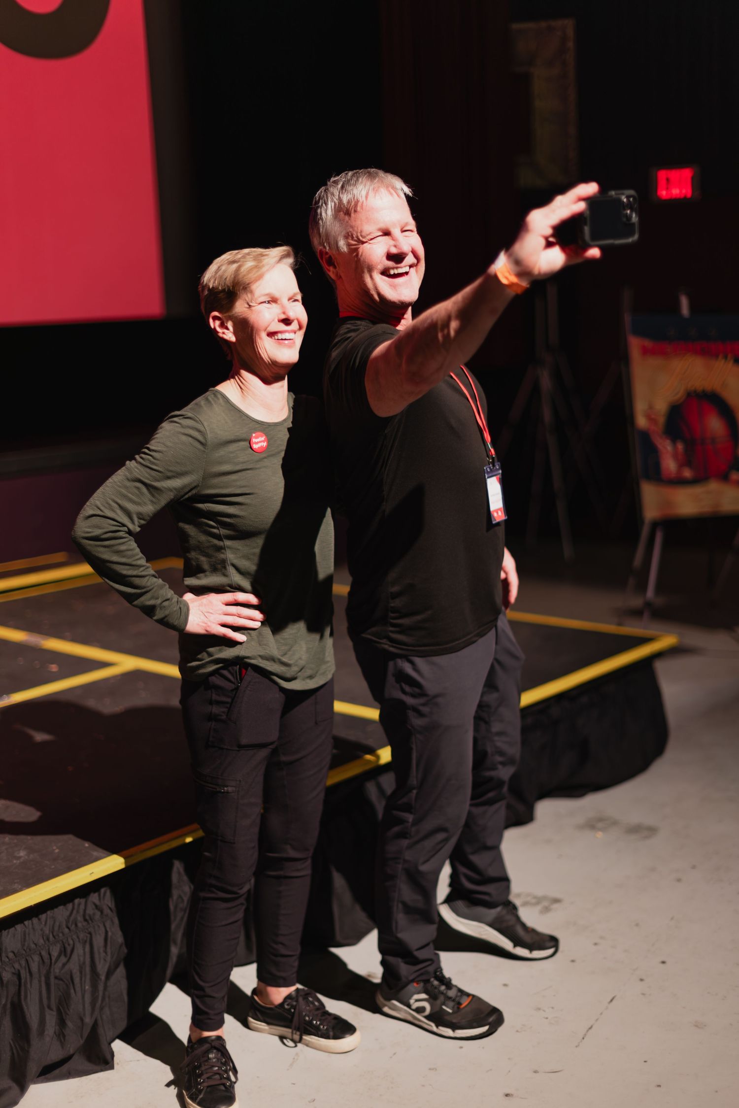 Man and woman taking selfie on stage at Spokane Film Festival event with red backdrop lighting.