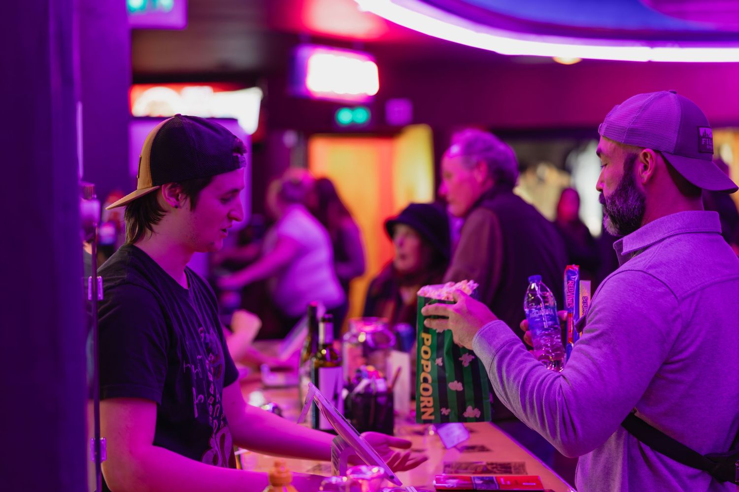 Bartender serving drinks to a bearded customer at a vibrant neon-lit bar.