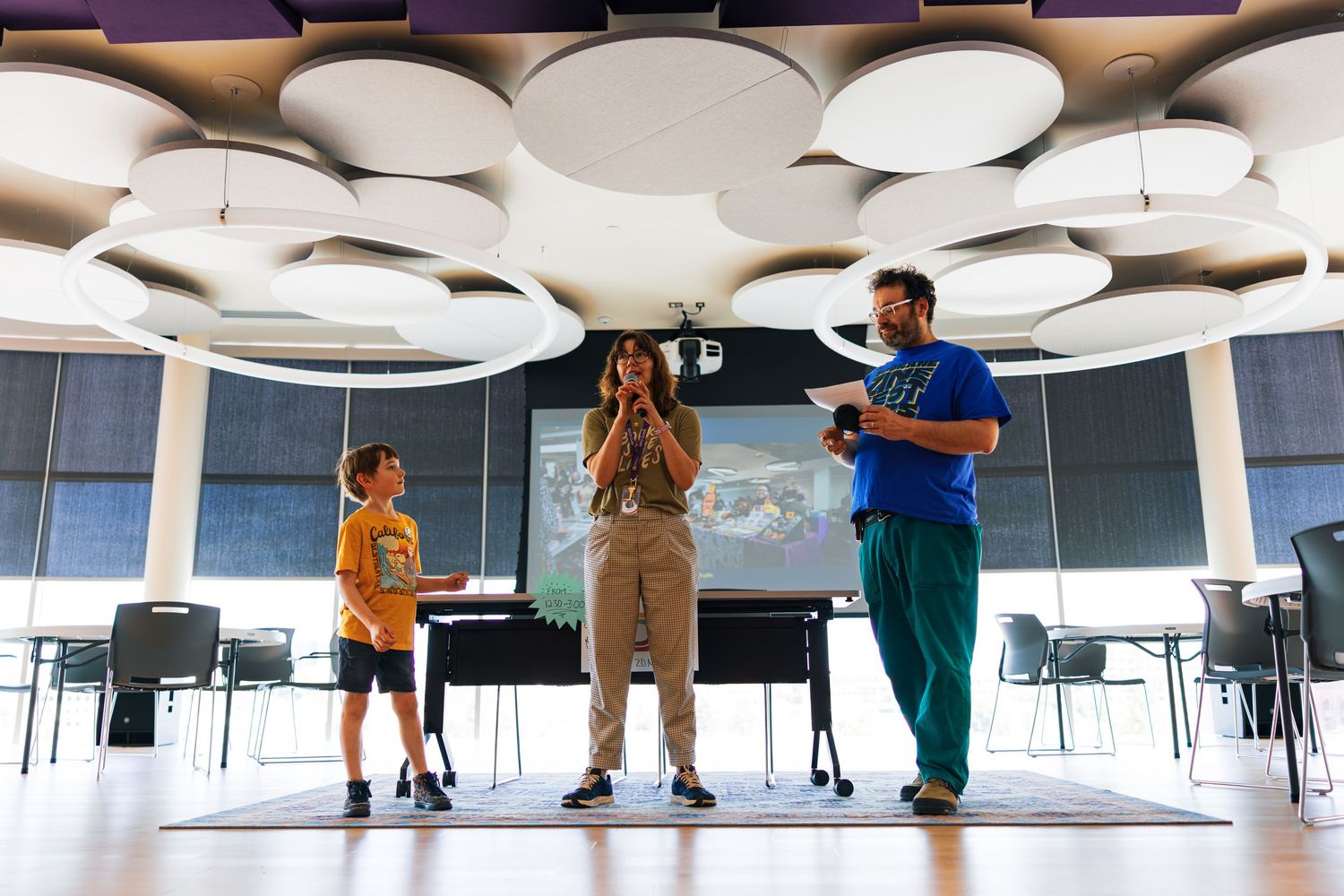 People practicing dance moves in a bright studio space with white circular ceiling lights and reflective floor.