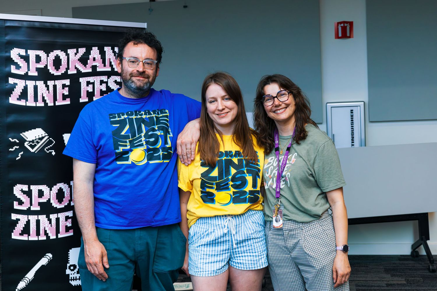 A group of people gather at a zine fest event with banners and displays visible in the background.