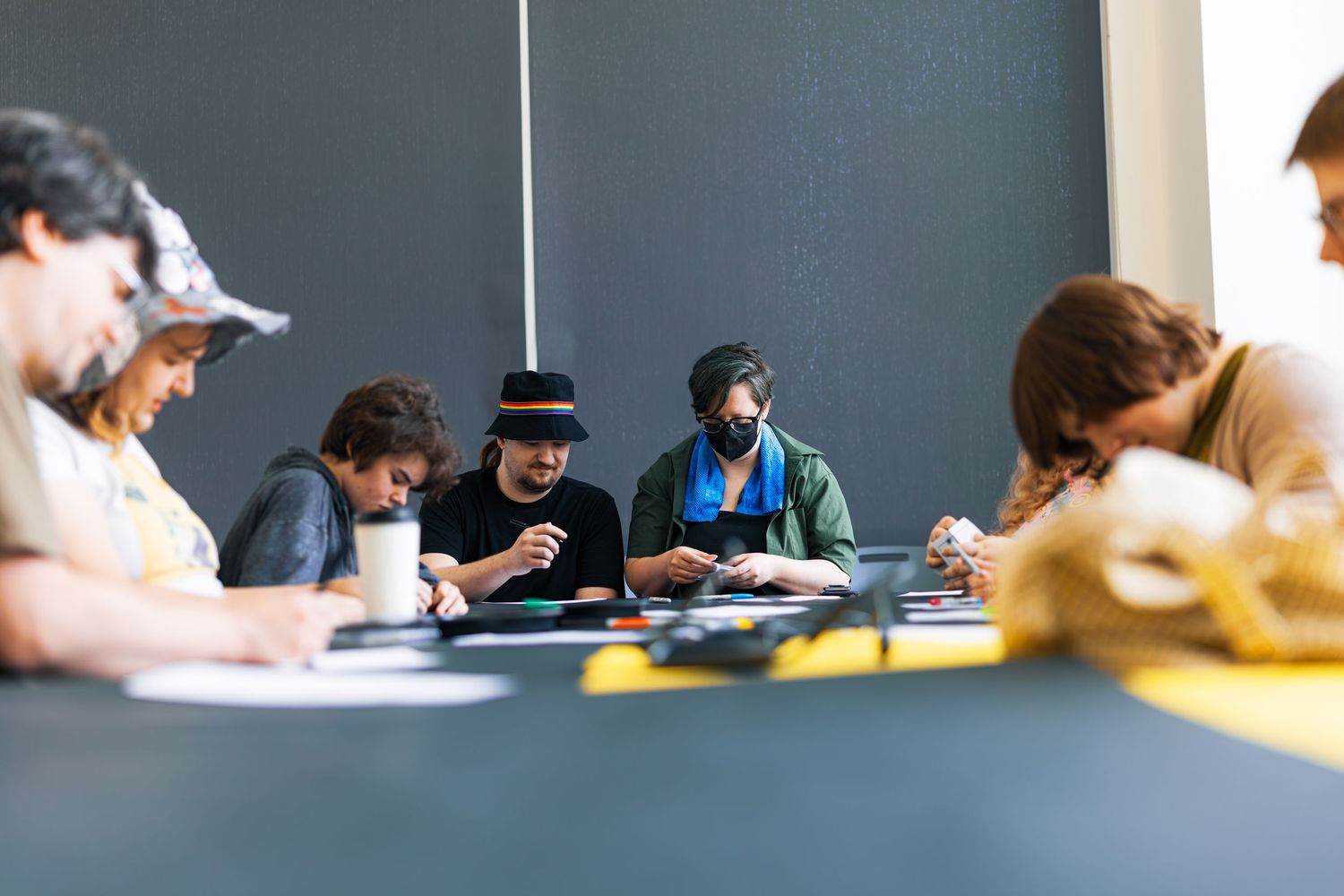 Students sit at desks in a classroom with dark walls while working on assignments and taking notes.