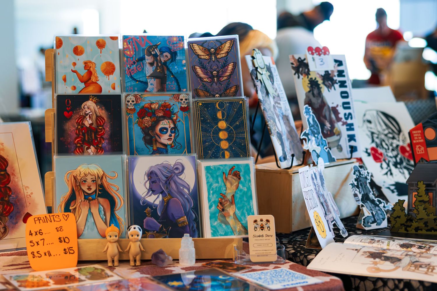 Colorful anime and fan art merchandise displayed at a convention or market stall with various prints and illustrations.