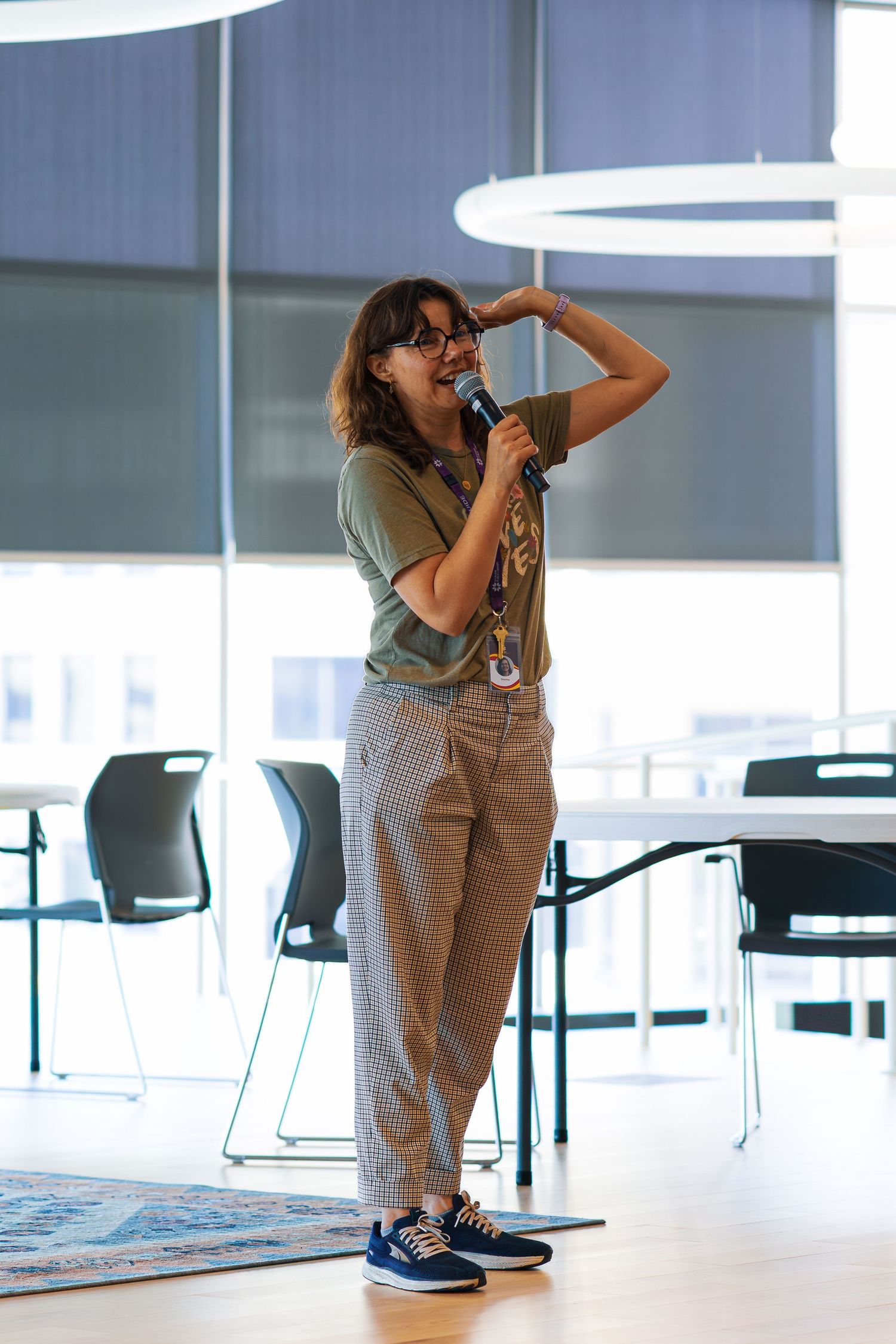 A person in overalls crouches and plays with a child in a bright modern office space with white chairs and tables.