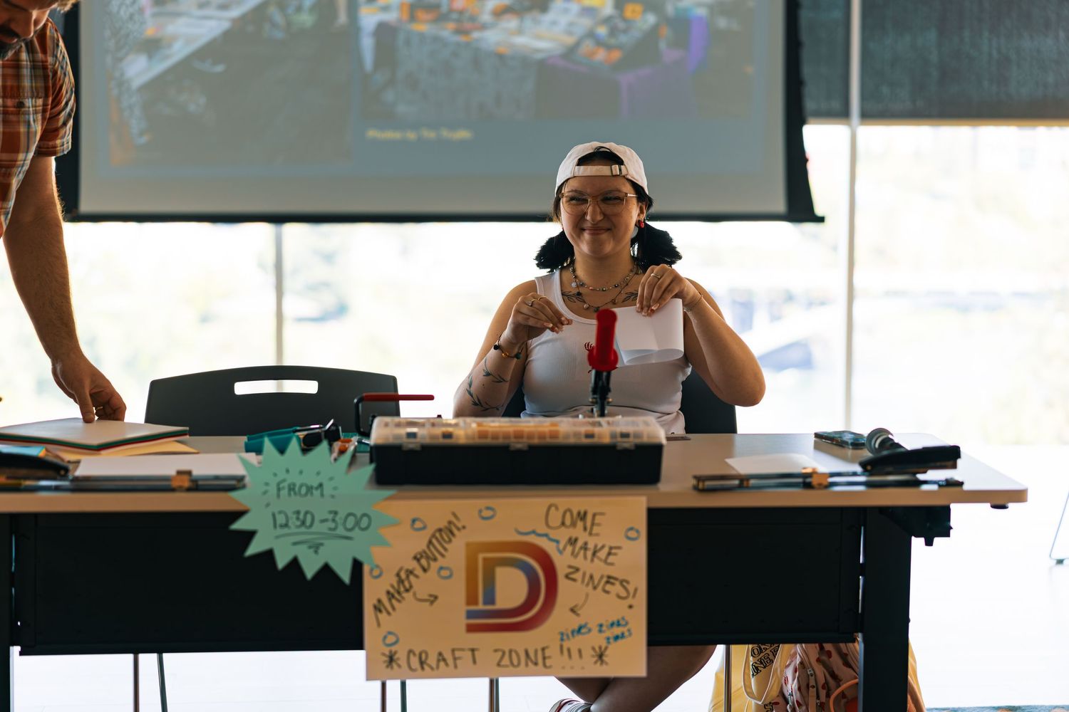 Someone sits at a desk with headphones during an event, with a decorated sign visible in the foreground.