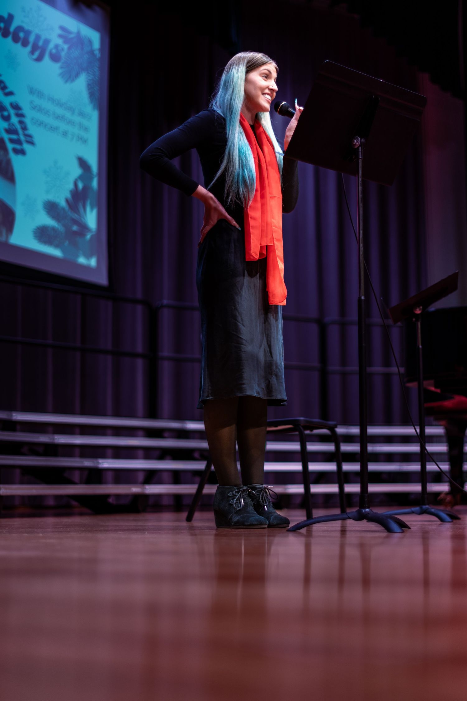 A performer in a red vest stands on a dark stage illuminated by blue lighting during a show.