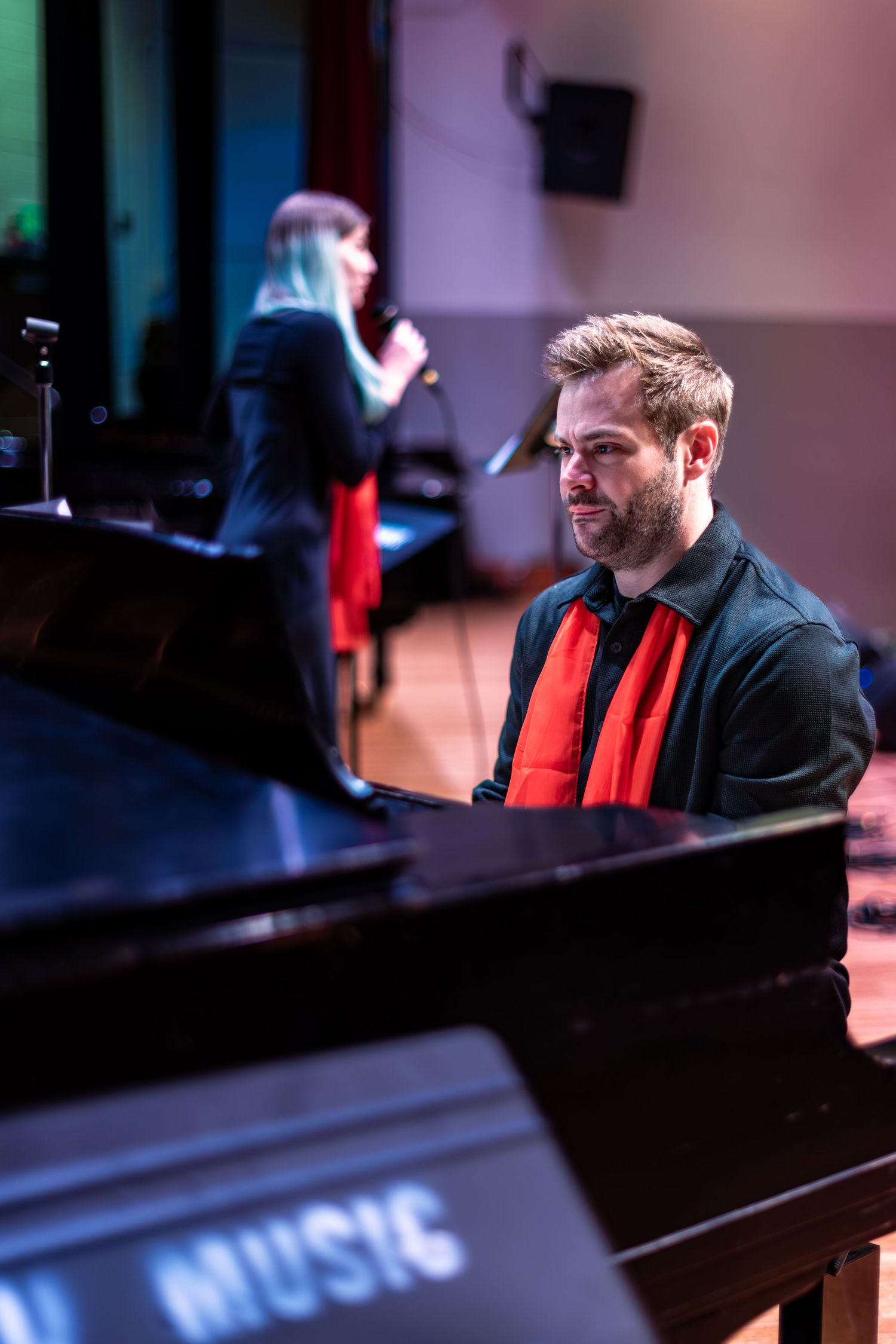 A pianist performs at a grand piano in a dimly lit venue with dramatic lighting creating an atmospheric ambiance.