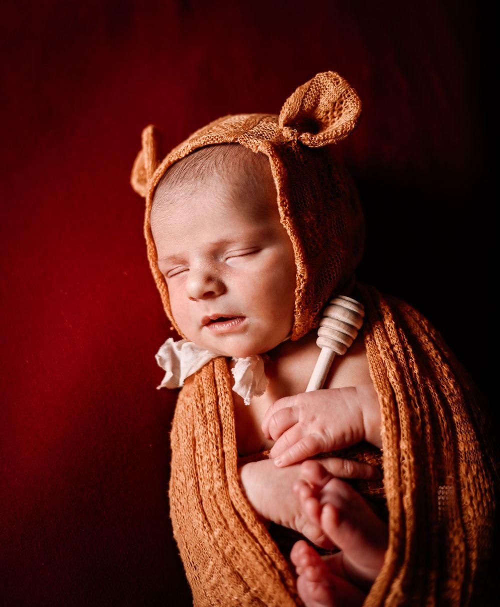 A sleeping newborn baby curled up in brown knit fabric against a dark background.