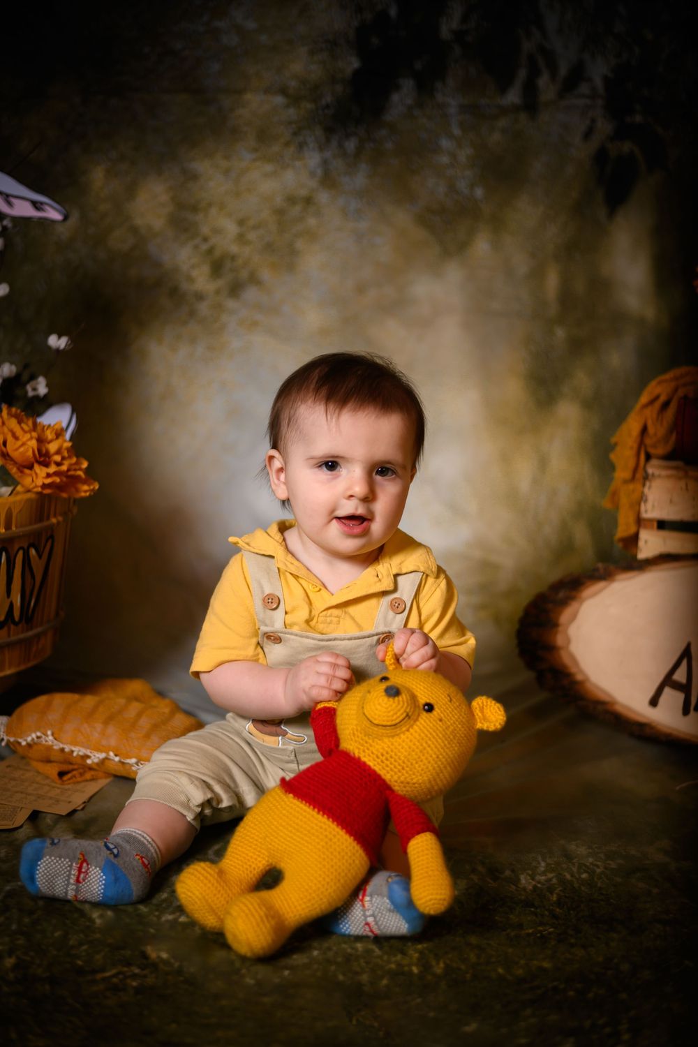 A small child in a yellow shirt plays with a plush Winnie the Pooh toy during a professional photo session.