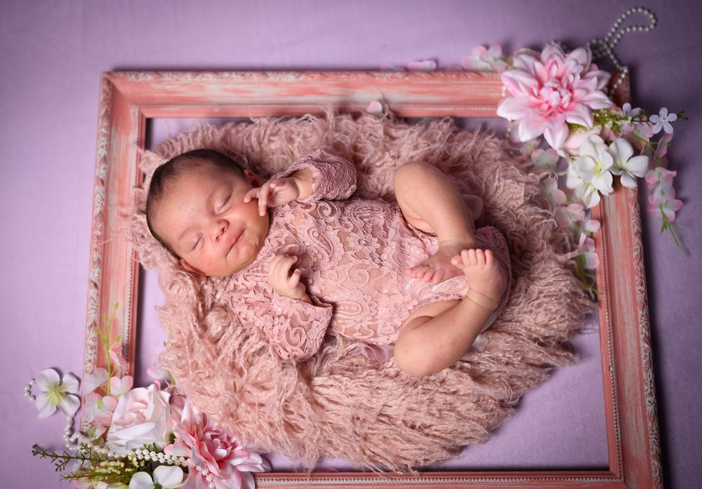 Sleeping newborn baby in pink swaddle blanket lying in decorative wooden frame with delicate floral accents.