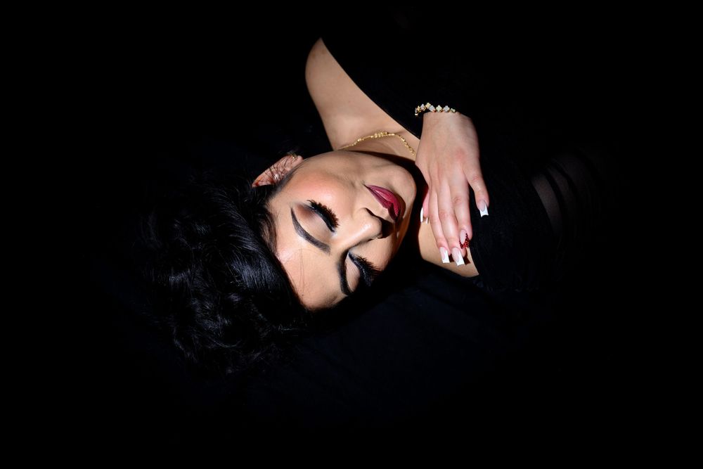 Dramatic portrait of someone lying against dark background with red lipstick and dark hair.