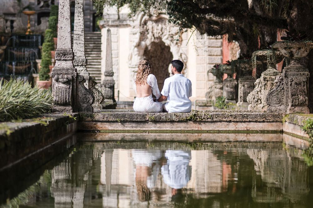 Couple sitting by water reflection during engagement photos at Vizcaya Museum