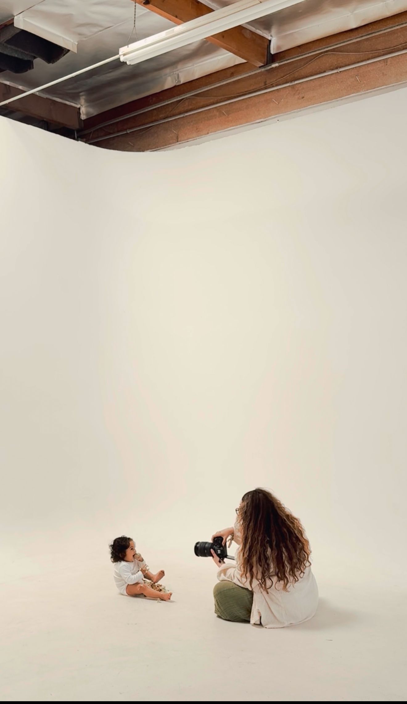 A photographer in a white studio space lies on the floor in different poses while taking photos with a professional camera.