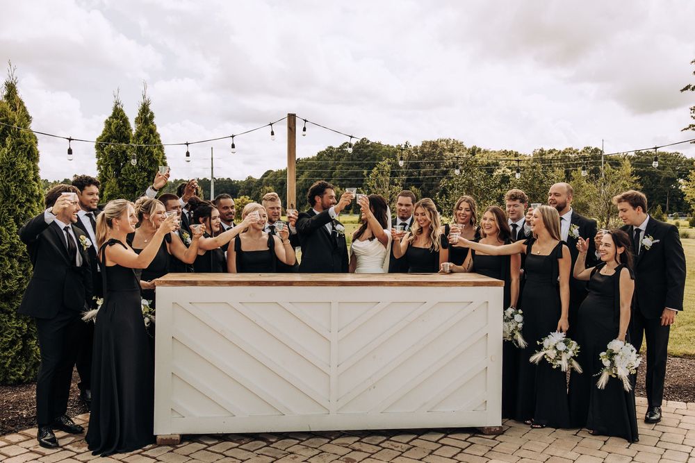 Bride and groom celebrate with large wedding party raising glasses at elegant outdoor bar.