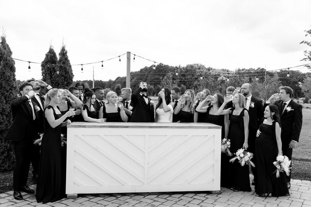 Black and white photo of wedding party toasting at chevron bar during outdoor reception.