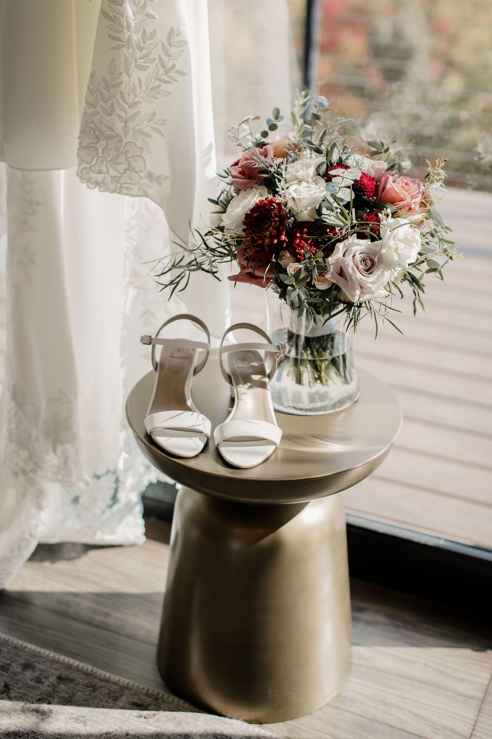 White bridal shoes and delicate floral arrangements displayed on a modern metallic side table.