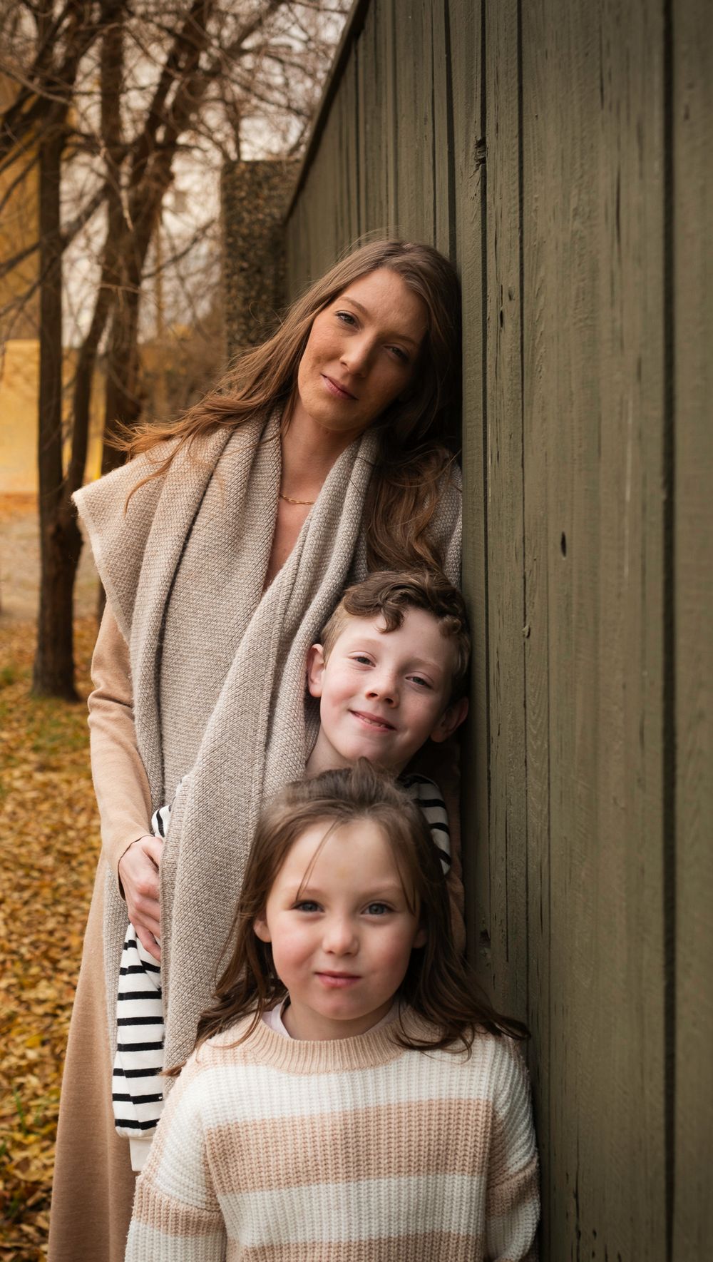 Family leaning against weathered green wall during autumn portrait session.